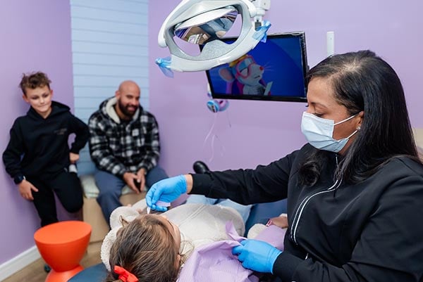A dental assistant with a kid cleaning their teeth