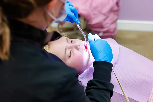 A dental hygienist cleaning a patient's teeth and preparing it for flouride treatment