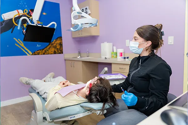 A dental hygienist at Howell Pediatric Dentistry sharing flossing tip with patient and parent
